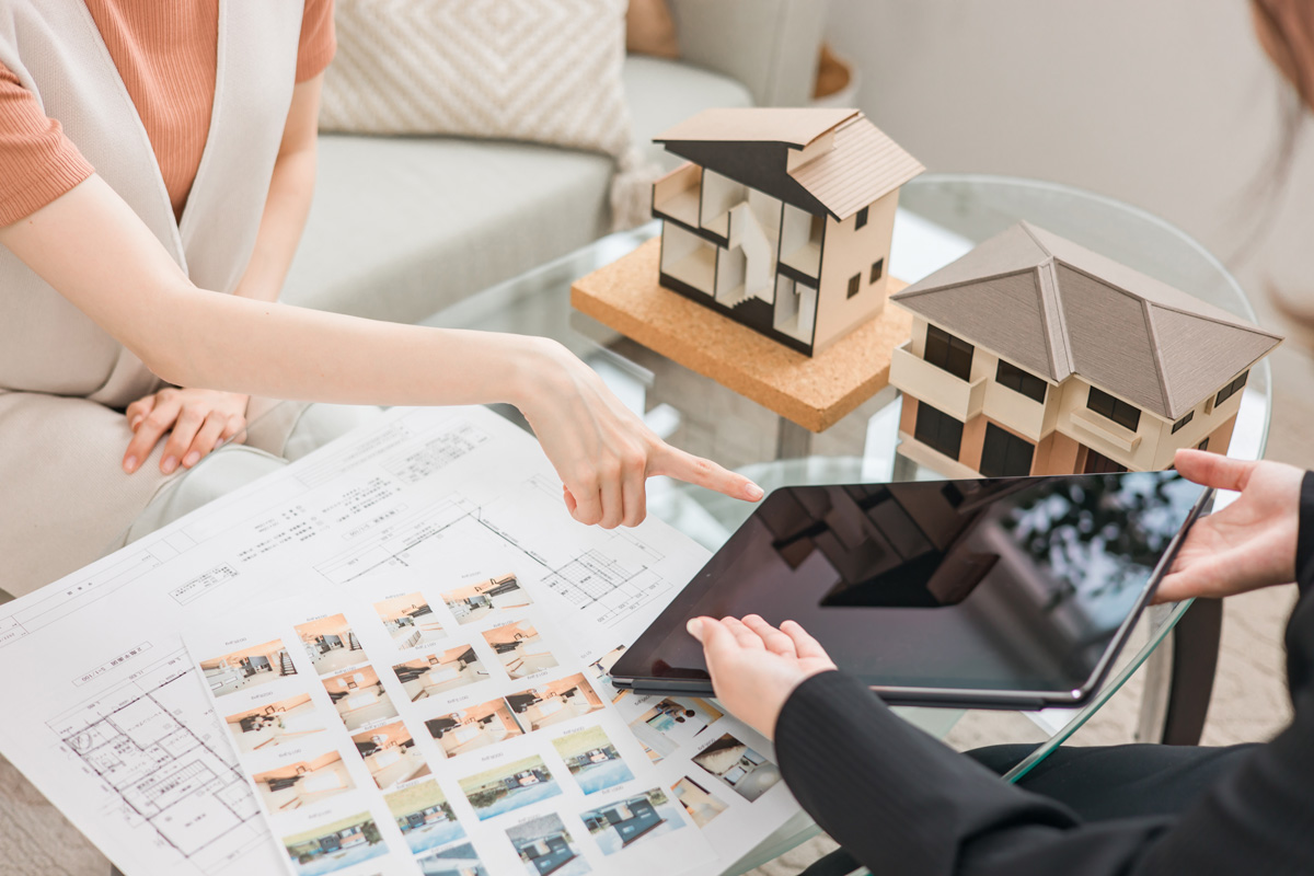 A person pointing to a tablet with small model homes and blueprints on the table.